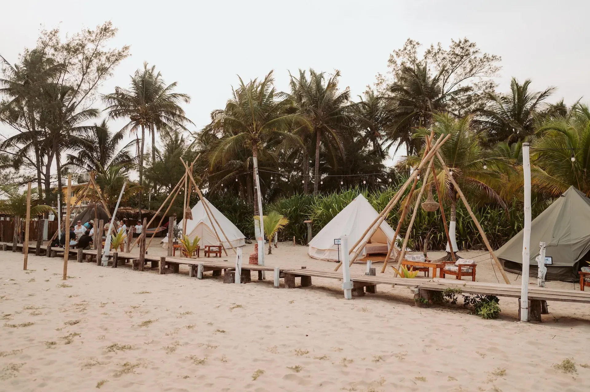 Bell tents lined up on the sand at Playa Azul, between palm trees and wooden walkways