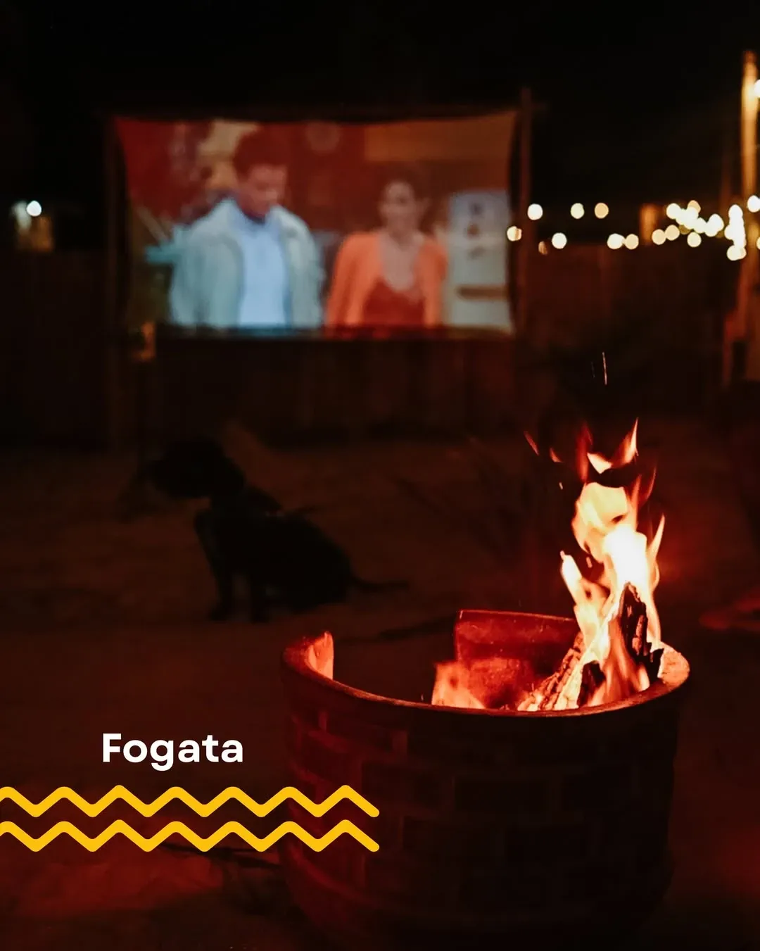The bonfire burning on the sand, with the film projected behind it