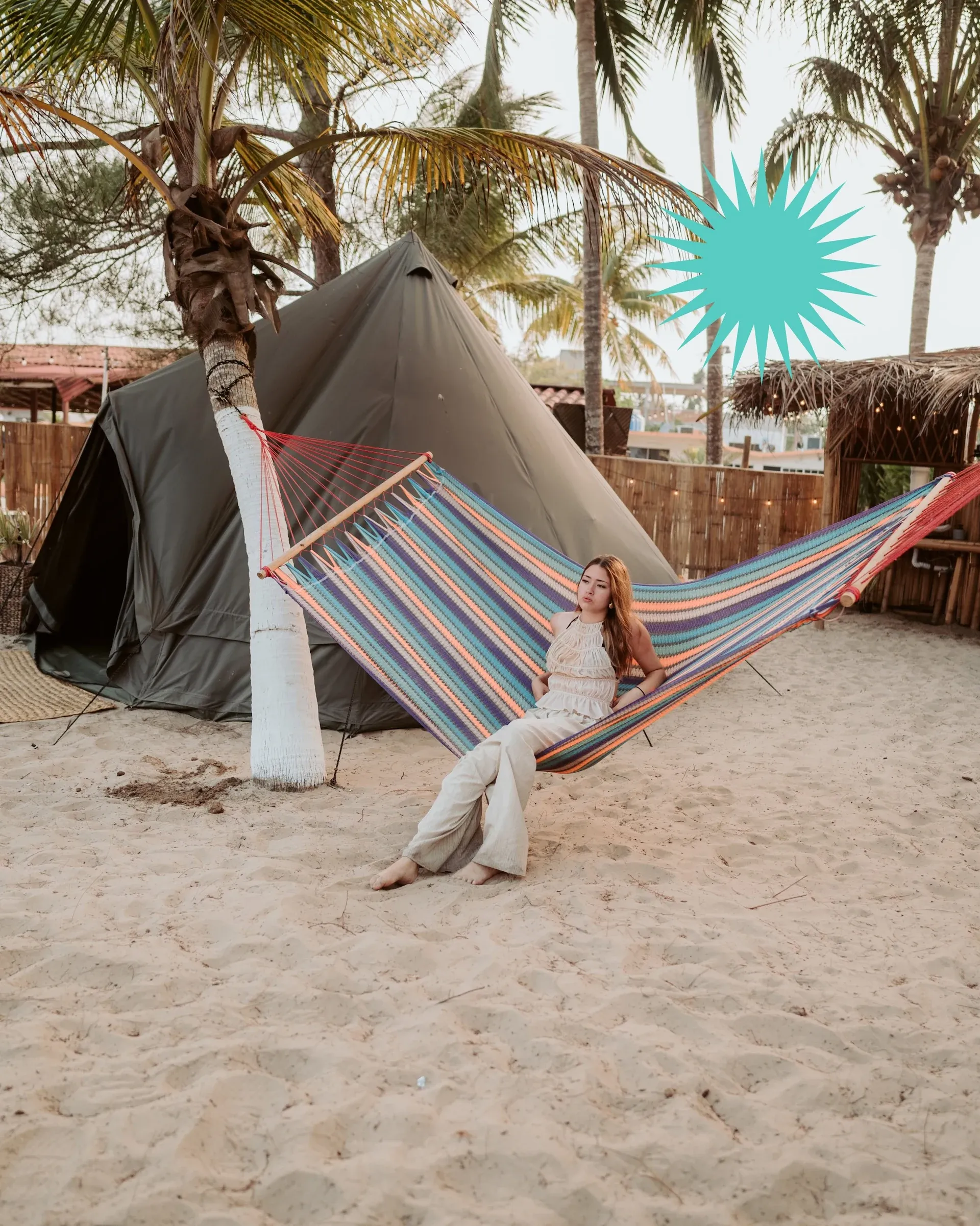 A guest resting in a striped hammock strung between palm trees, next to the tents