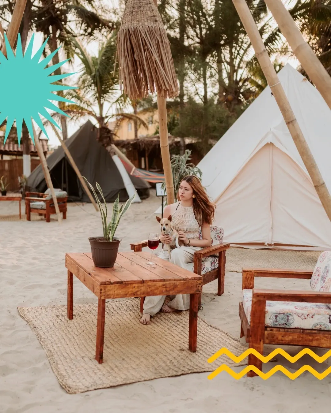 Lounge area on the sand with a wooden table, armchairs and a dog beside its owner