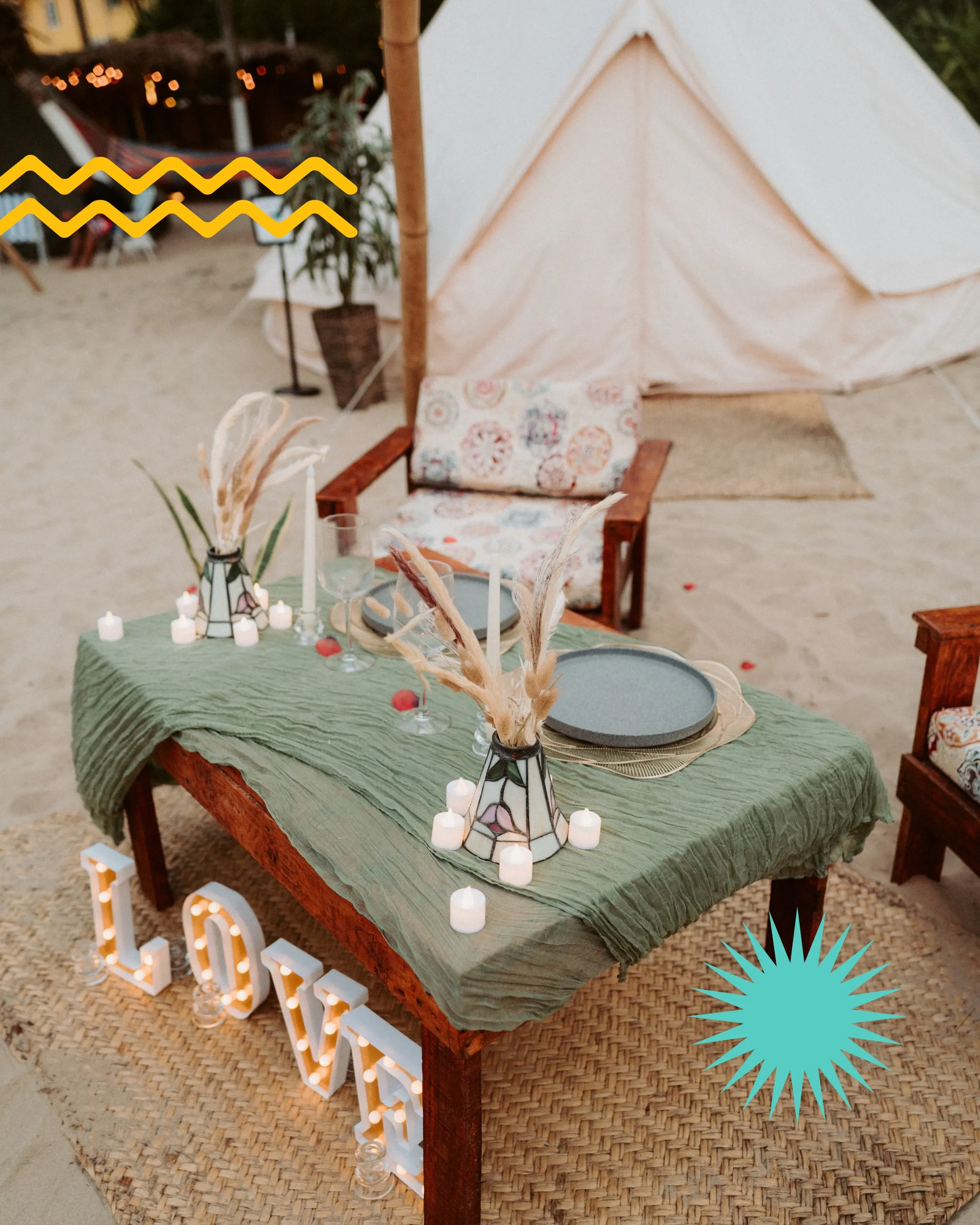 A table set for a birthday dinner with a green cloth, candles and tableware on the sand