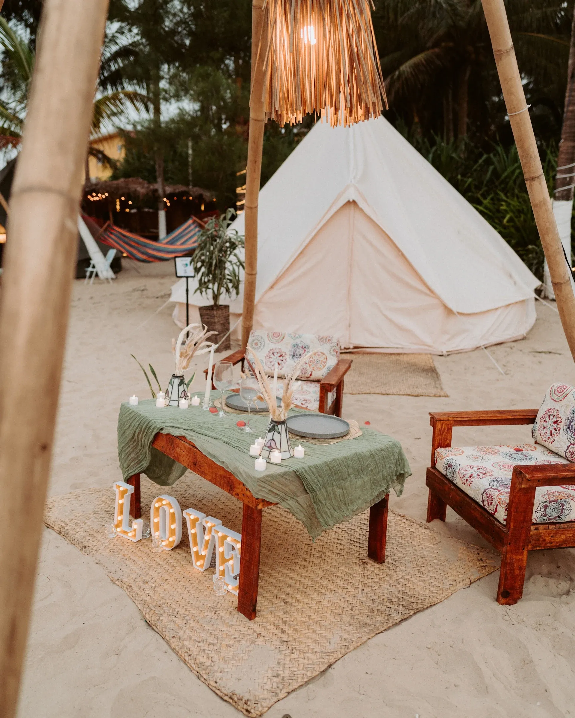 A tent set up for a marriage proposal, with candles, dried flowers and LOVE letters on the sand