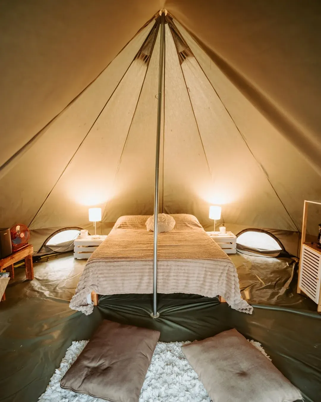 Inside a traditional tent with made-up beds, a rug and warm lamps switched on