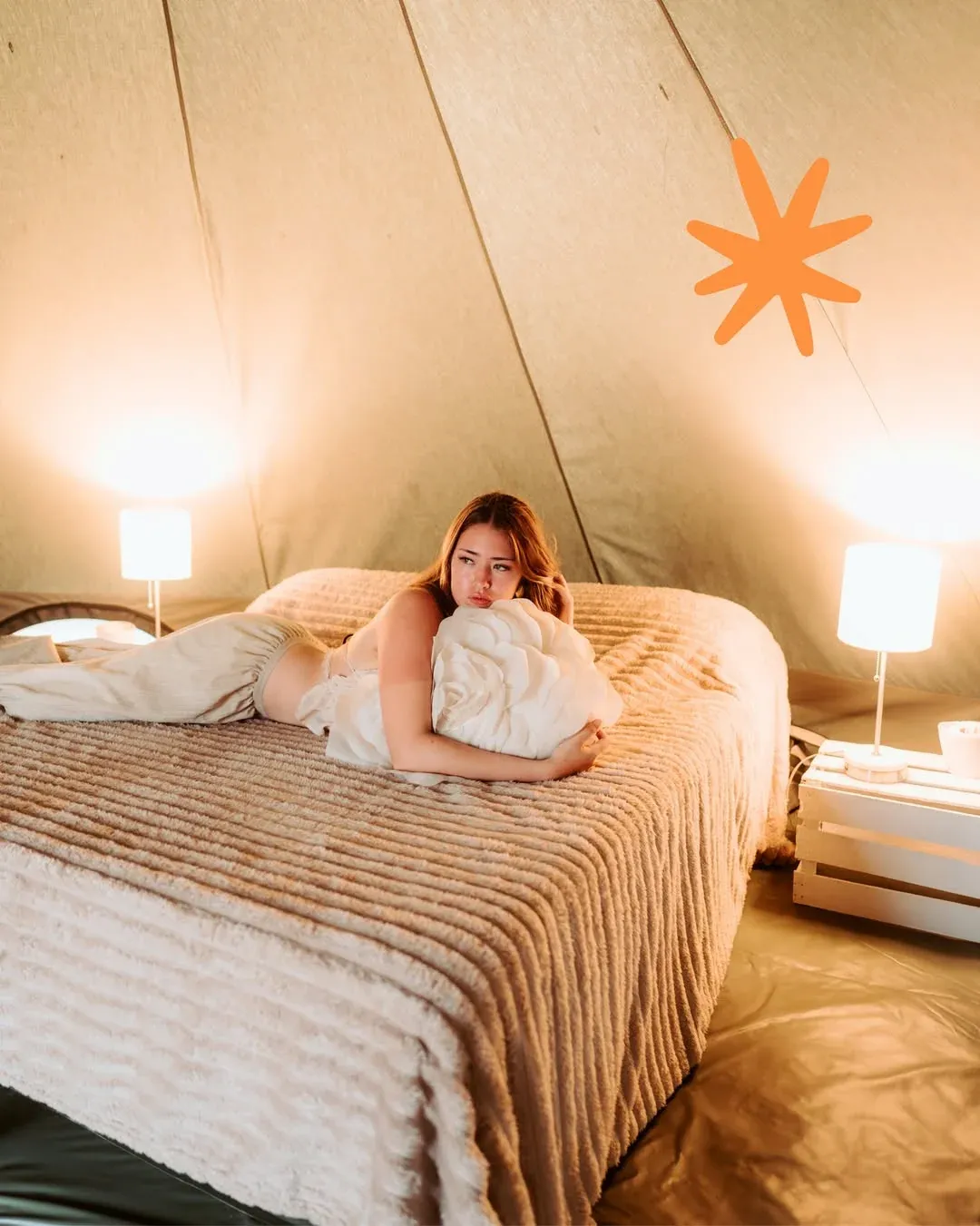 Inside the VIP tent with a king bed, bedside lamps and warm-toned bedding